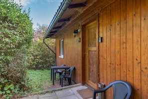 A wooden building with a door, a window, and a table with chairs outside.