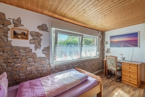 Ein Schlafzimmer mit Steinsandsteinwand, einem Bett, einem Schreibtisch und einem Fenster mit Vorhängen.