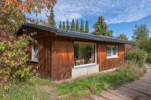Eine Holzhütte mit einem großen Fenster und einer Tür, umgeben von Bäumen und einem Steinweg.