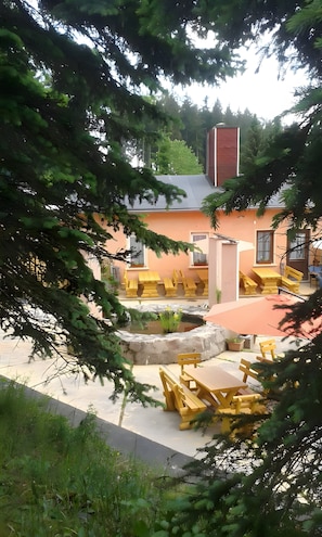 Ein Innenhof mit gelber Außenbestuhlung, einem kleinen Teich und einem Gebäude mit roter Fassade.