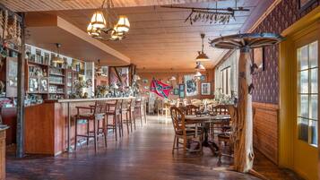 Angolo bar con pavimento in legno, diversi tipi di sedute e scaffali pieni di bottiglie e bicchieri.