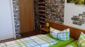 A room with two beds, a brick wall, a wooden door, and a small table with a lamp.