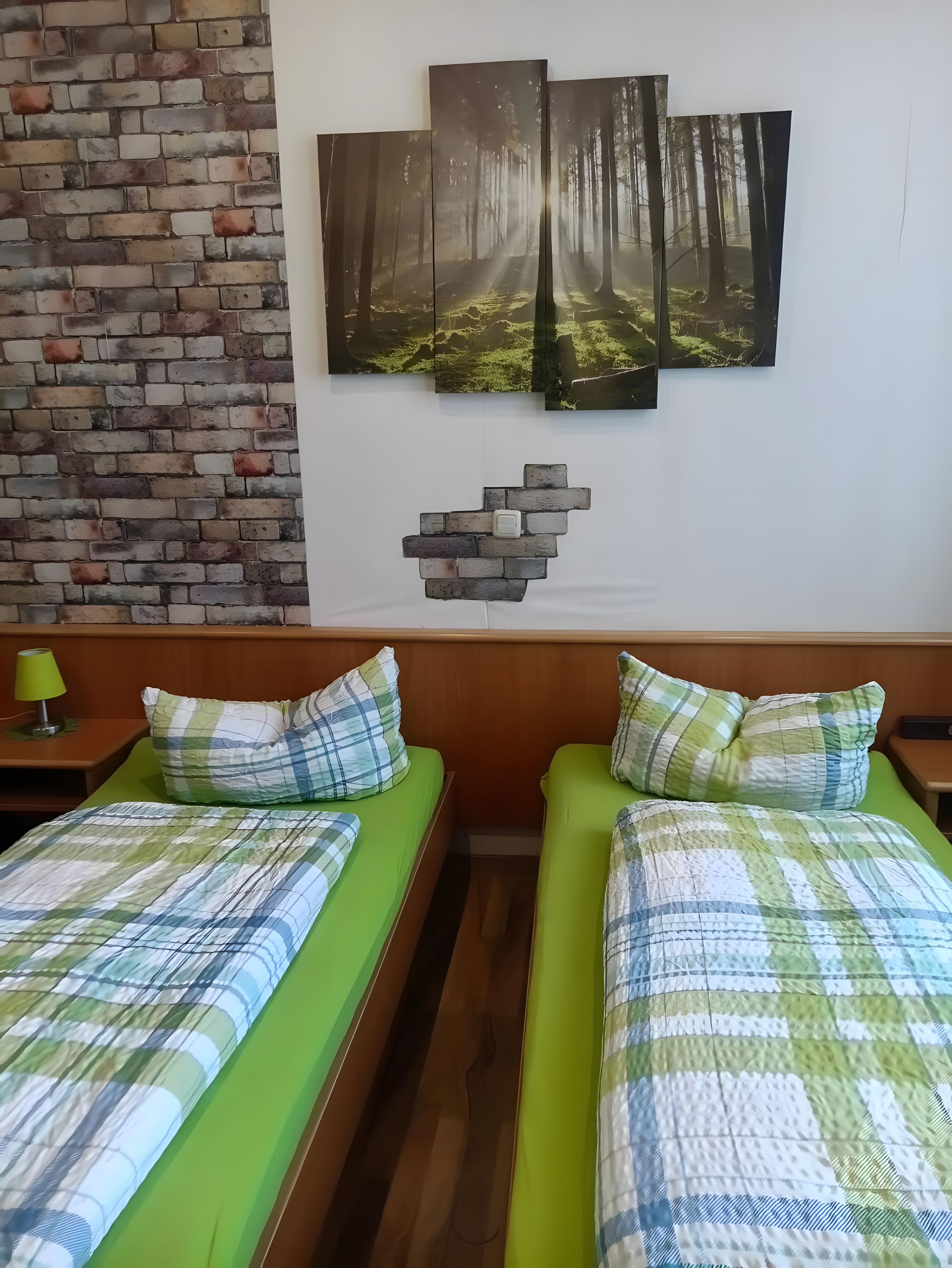 A room with two beds, a brick wall, and a forest-themed artwork.