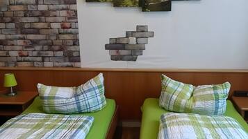 A room with two beds, a brick wall, and a forest-themed artwork.