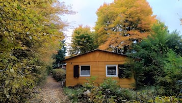 Una petita cabana de fusta amb un camí de grava que hi mena, envoltada de fullatge d'autumn.