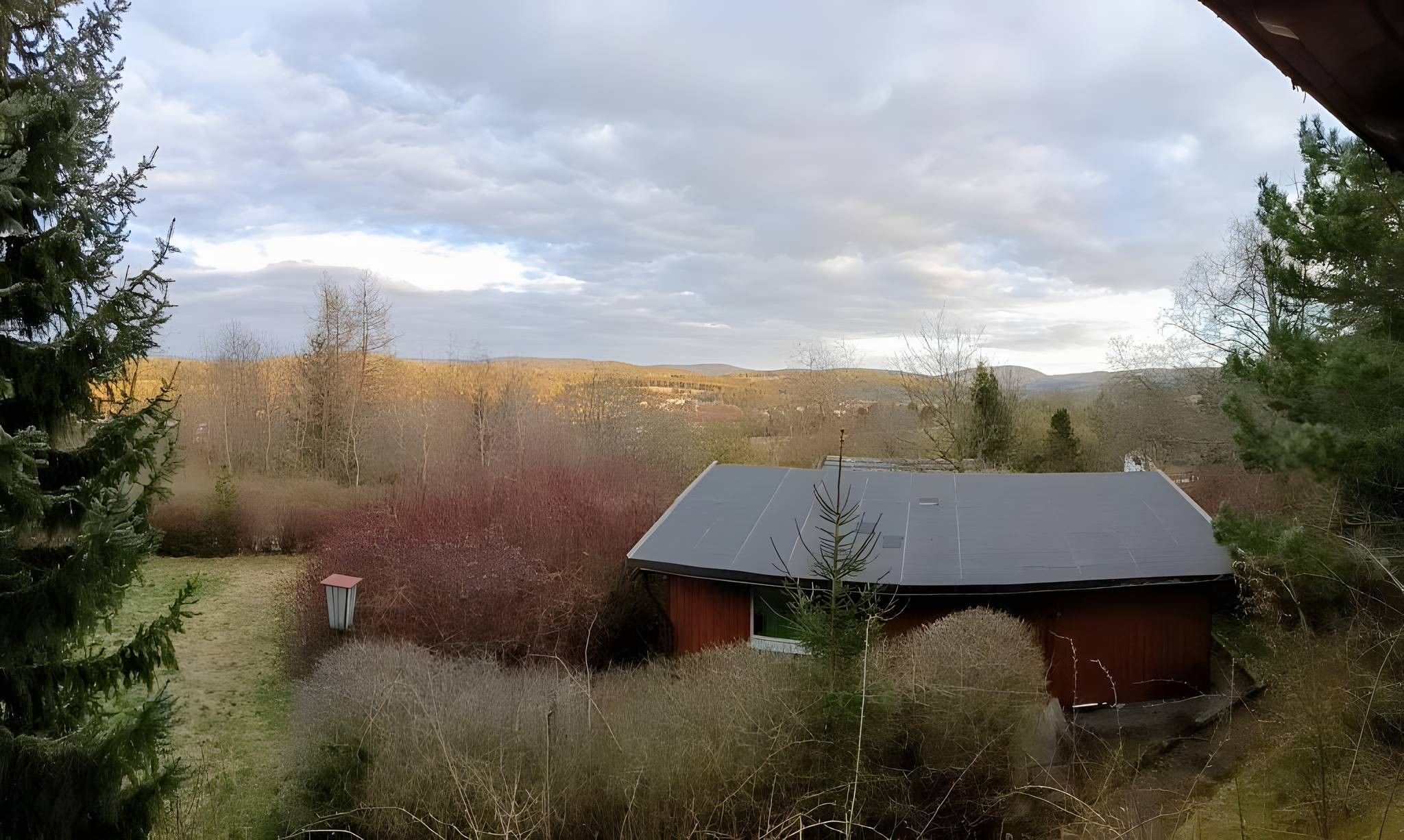 Une maison avec un toit en pente, entourée d’une végétation luxuriante et sous un ciel dégagé.