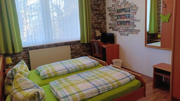 Een kamer met twee bedden, een bakstenen muur, een raam met gordijnen, een televisie en een spiegel.