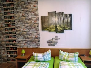 Ein Zimmer mit Backsteinwand, einem Bett mit grüner Bettwäsche und einem an der Wand befestigten Regal mit Topfpflanzen.