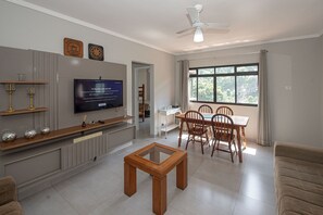 Una sala de estar con televisor, muebles de madera, una mesa de centro de vidrio y un comedor con sillas y mesa.