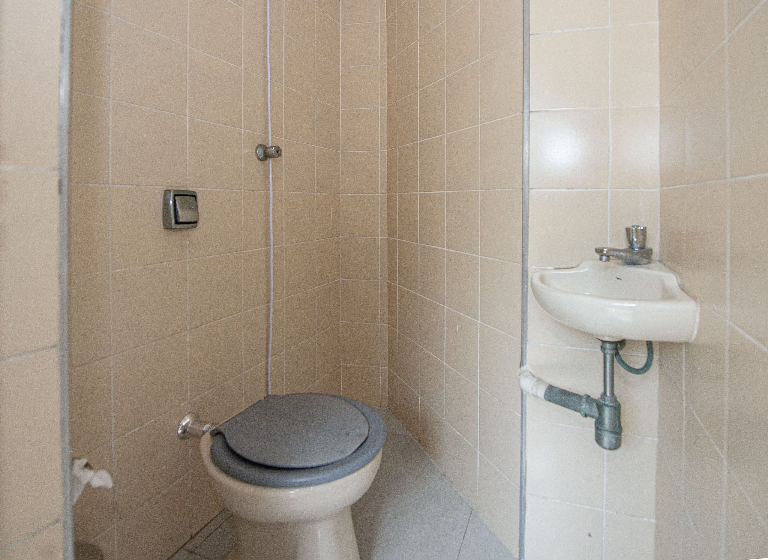 Une petite salle de bain carrelée, équipée de toilettes et d’un lavabo.