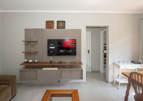 A living room with a flat-screen TV, wooden entertainment unit, and a sign that reads 'WELCOME TO THE TIKI BAR'.