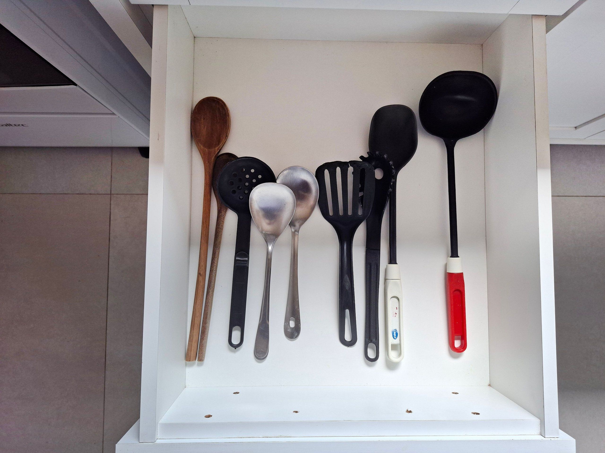 A kitchen drawer with various utensils including wooden spoons, black spatulas, and a ladle.