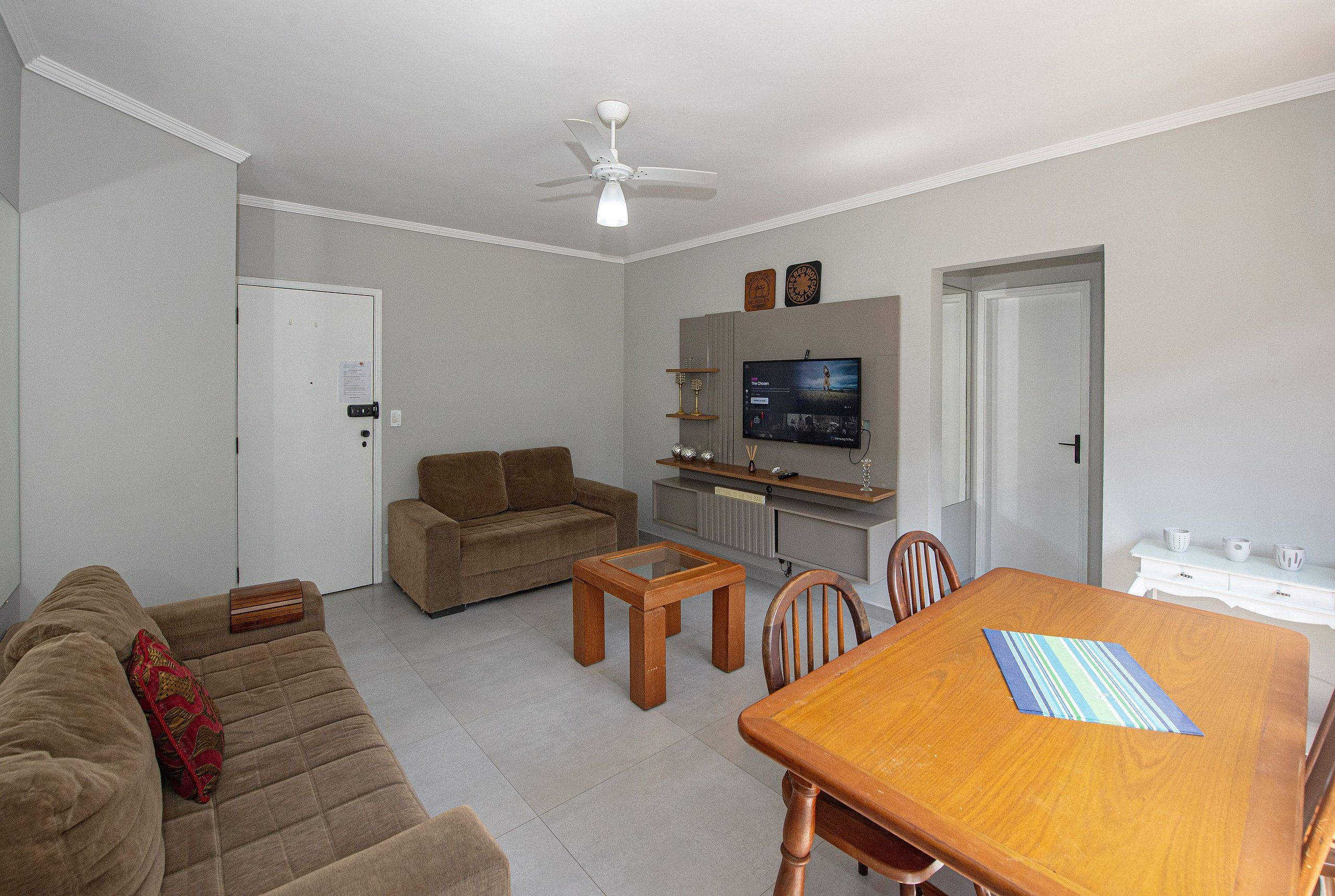 A living room with a sofa, a coffee table, a dining table, and a television.