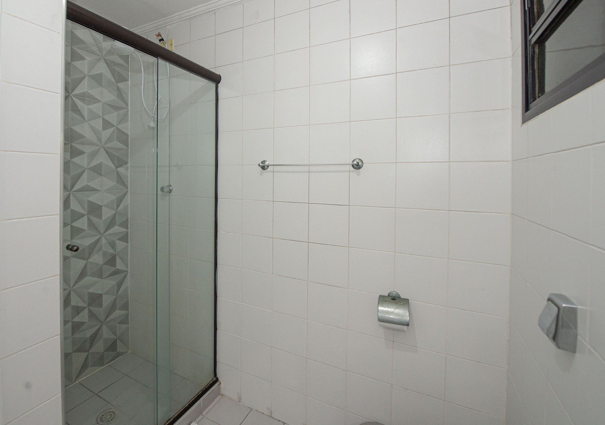 A bathroom with a glass shower enclosure, white tiled walls, and a towel rack.