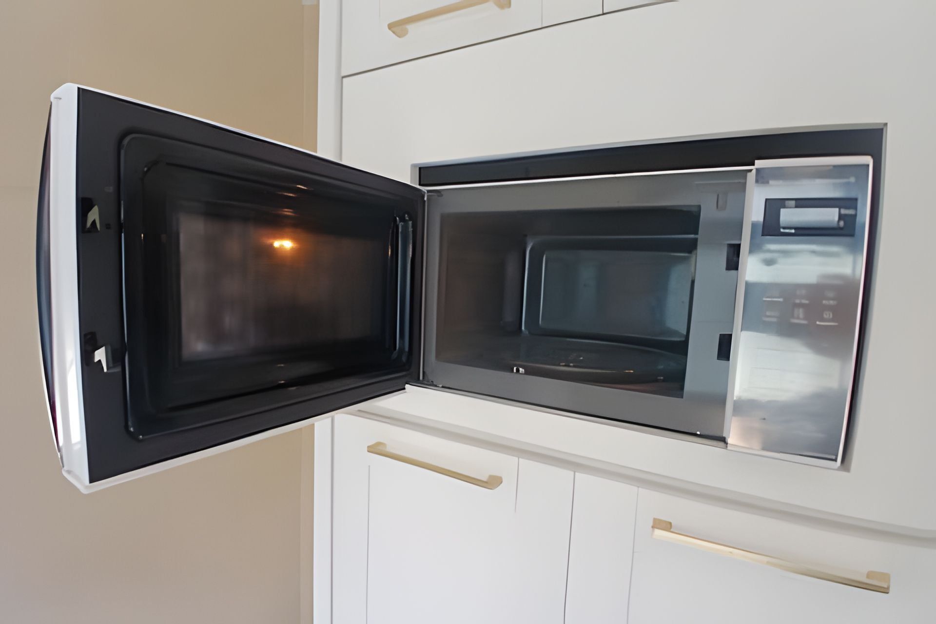 An open microwave in a kitchen with white cabinets and wooden handles.
