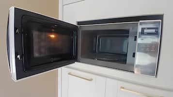 An open microwave in a kitchen with white cabinets and wooden handles.