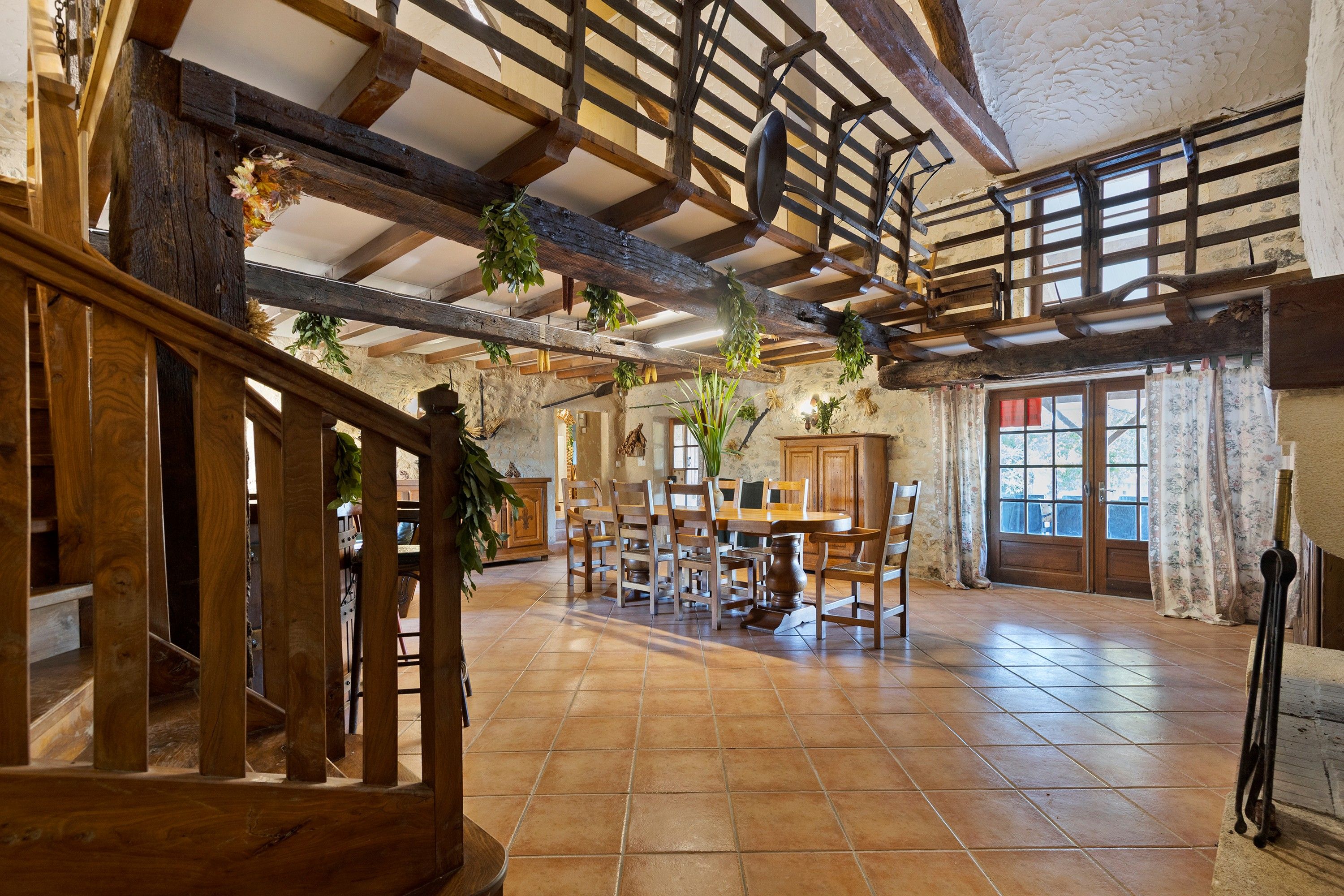 A rustic interior with exposed wooden beams, a dining area with wooden furniture, and a staircase with a wooden railing.