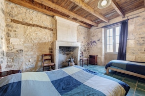 Ein rustikaler Raum mit freiliegenden Steinwänden, einer Holzbalkendecke, einem Bett mit blauer und weißer Steudecke, einem Stuhl und einem kleinen Tisch.