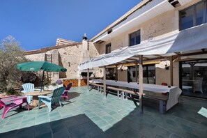 An outdoor patio with tables and chairs, a stone building in the background, and a clear blue sky. - Charming Winegrower's House with Lake View, Private Pool, and Wi-Fi (Guizengeard)
