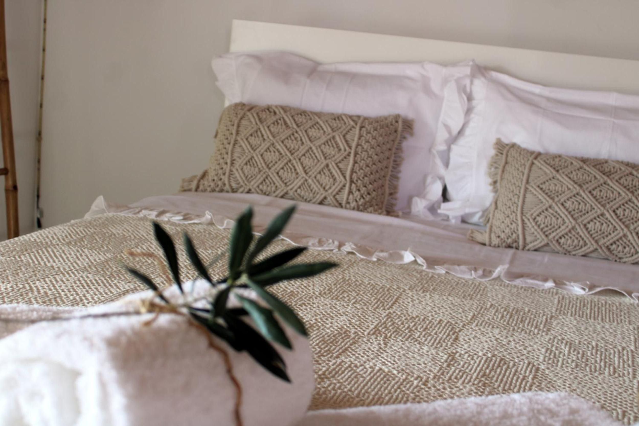 Ein Bett mit einer strukturierten Decke, einem Kissen mit geometrischem Muster und einer Pflanze im Topf.