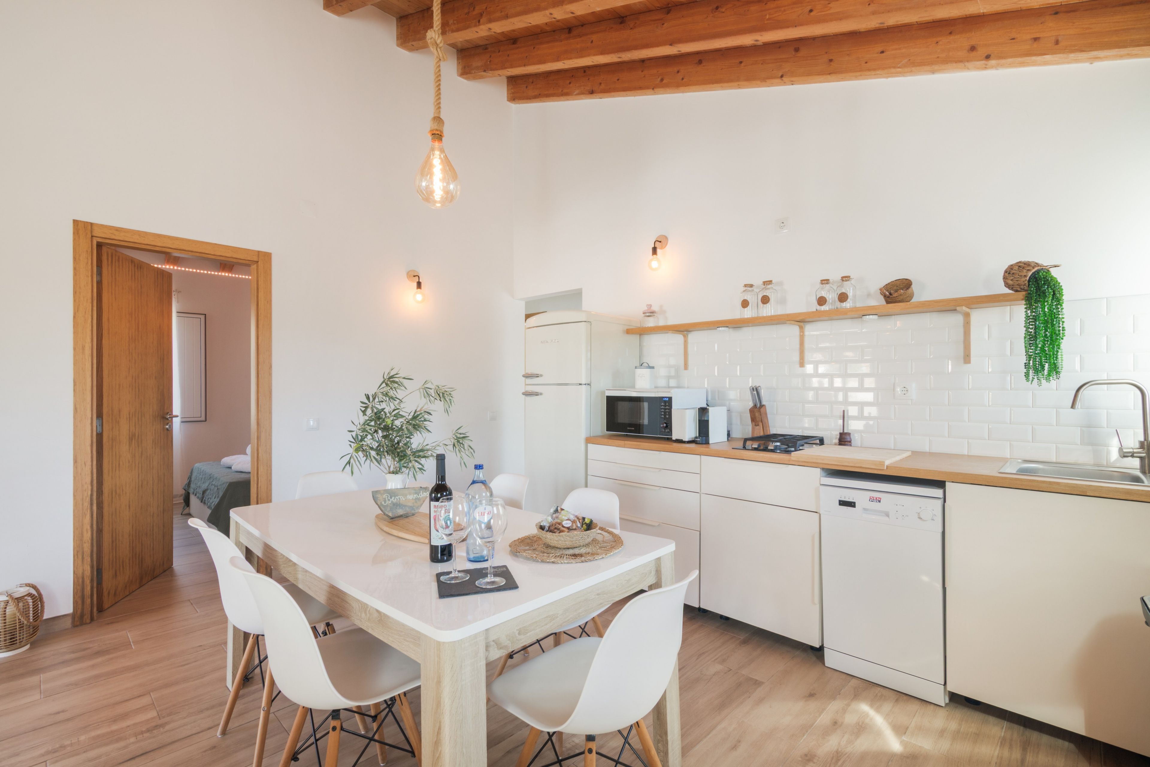 Une cuisine moderne avec des meubles blancs, un plan de travail en bois et un coin repas comprenant une table et des chaises.