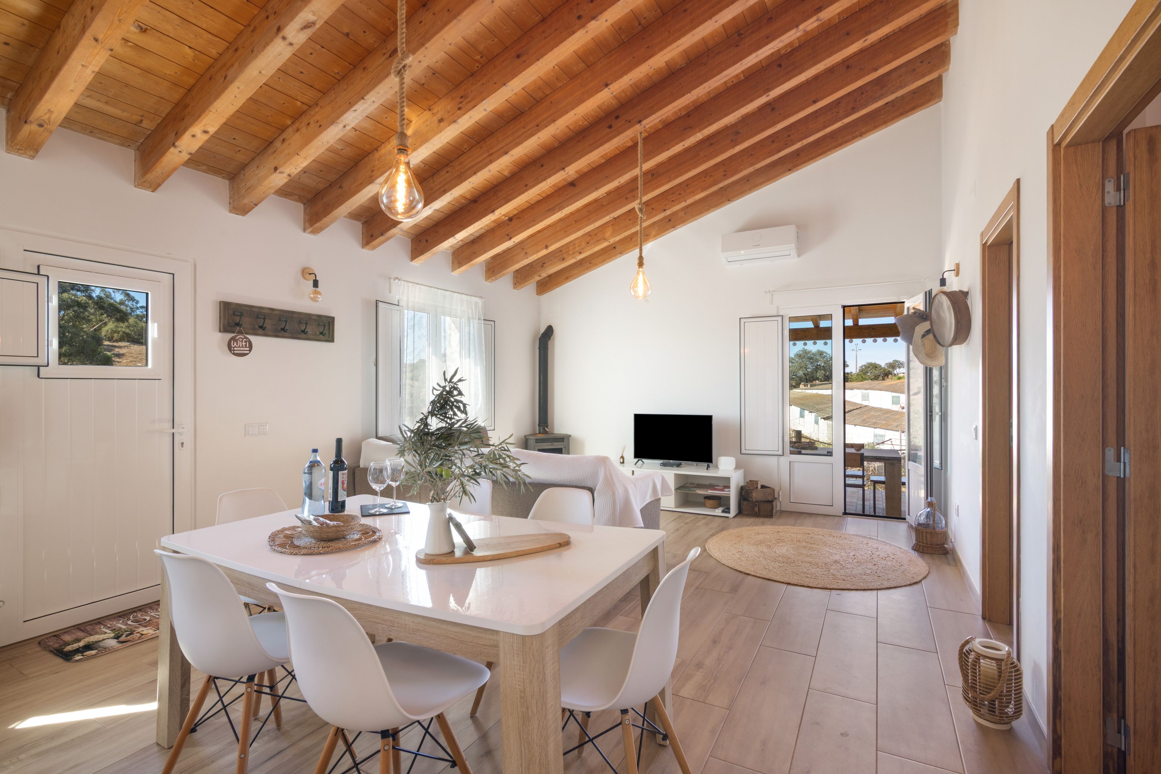 A modern kitchen with wooden beams, a dining table with chairs, a TV, and a view of the outdoors.