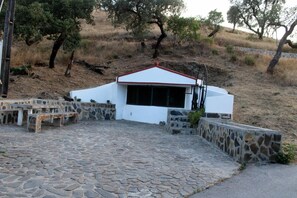 A stone-paved patio with a white building featuring a red roof, surrounded by stone walls and benches. - Holiday Home 'Casa Dos Currais' with Mountain View, Wi-Fi and Air Conditioning (Cachopo)