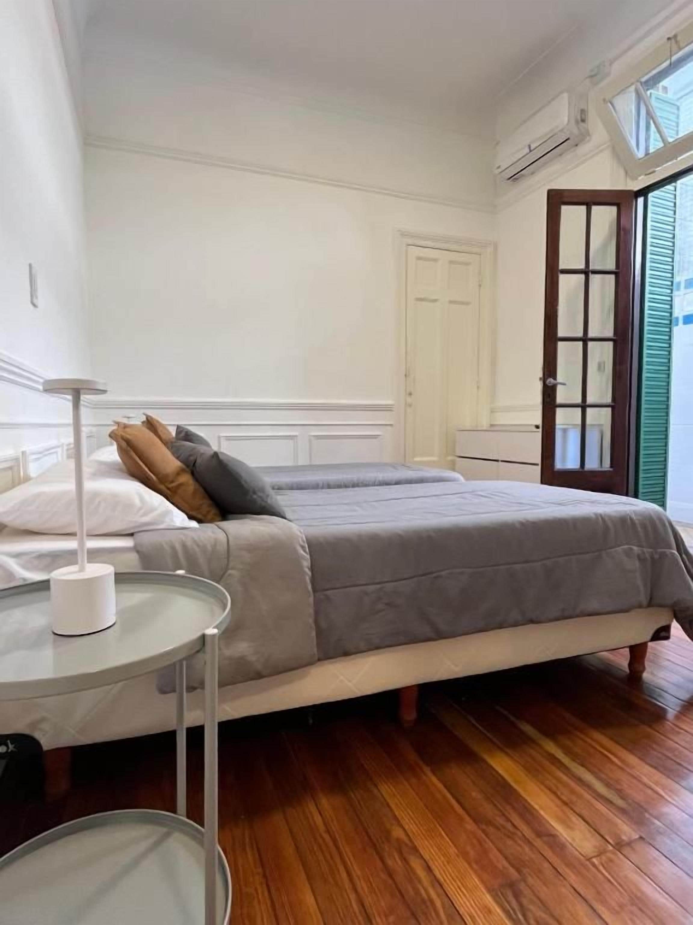 Un dormitorio con dos camas, una mesita de noche con lámpara, suelo de madera y una ventana con vistas.