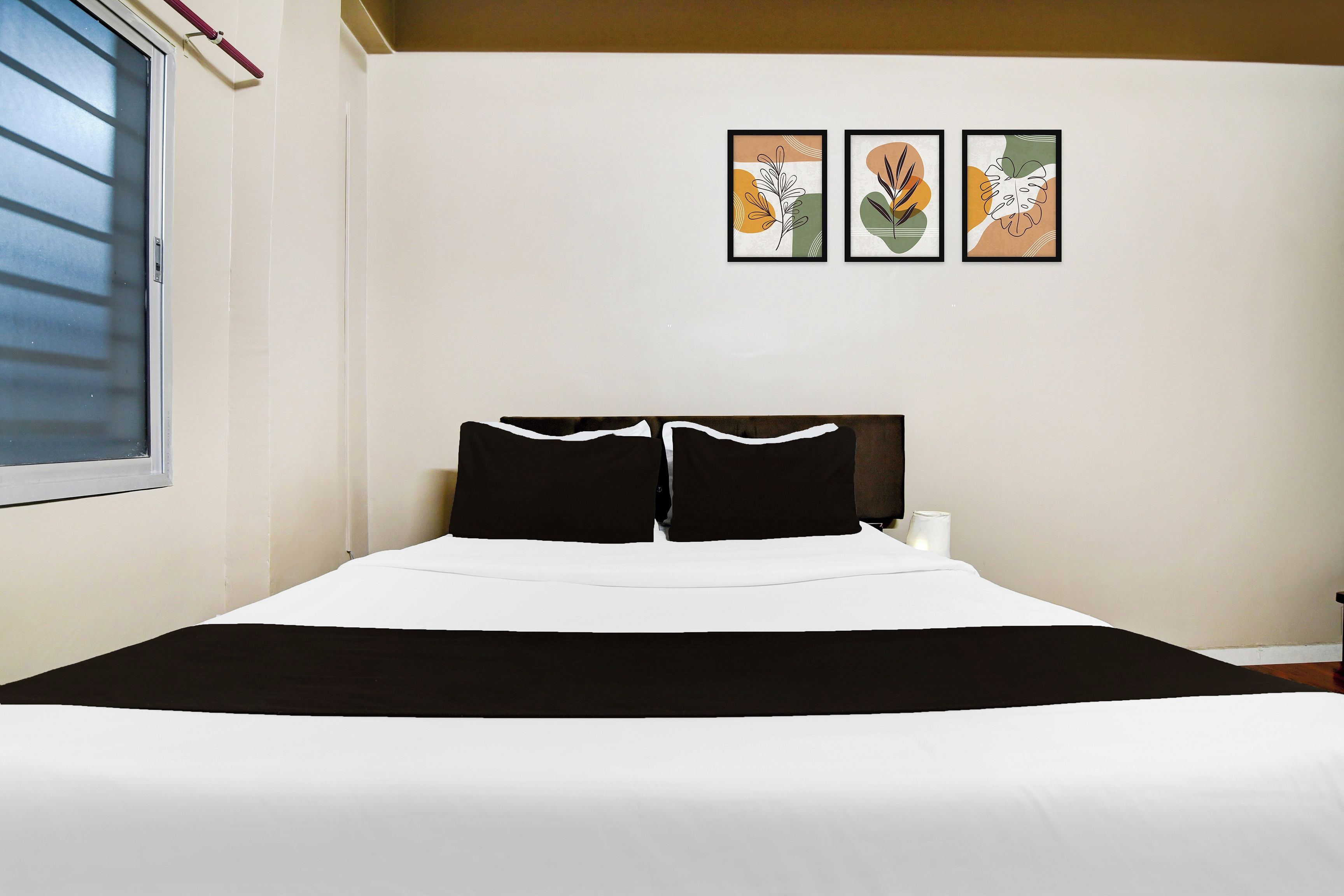 A bed with a black and white bedspread, two black pillows, and a headboard. There are three framed artworks on the wall above the bed.