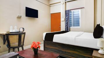 A hotel room with a bed, a desk with a chair, a television, an air conditioning unit, and a window with curtains.