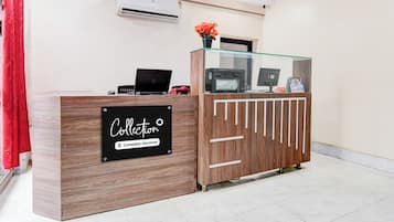 A reception desk with a sign indicating it's company-serviced, a laptop, a printer, and a vase with flowers.