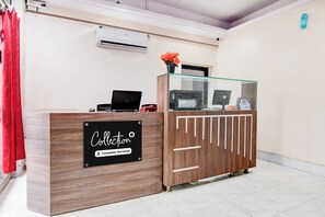 A reception desk with a sign indicating it's company-serviced, a laptop, a printer, and a vase with flowers.