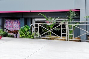 A gated entrance with a metal gate, potted plants, and a staircase leading to a building with a pink awning.