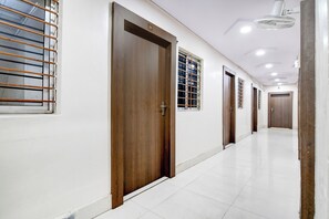 Un couloir avec des portes et des fenêtres en bois, un sol carrelé de carreaux blancs et un ventilateur de plafond.