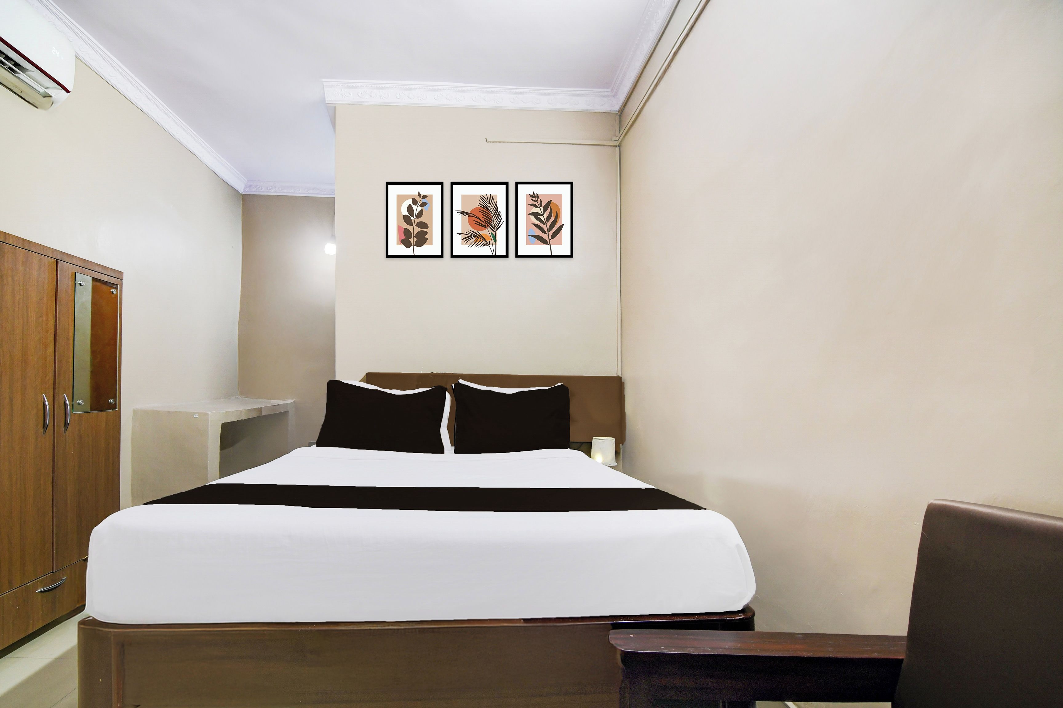 Una habitación de hotel con una cama, un escritorio, un armario y tres cuadros en la pared.