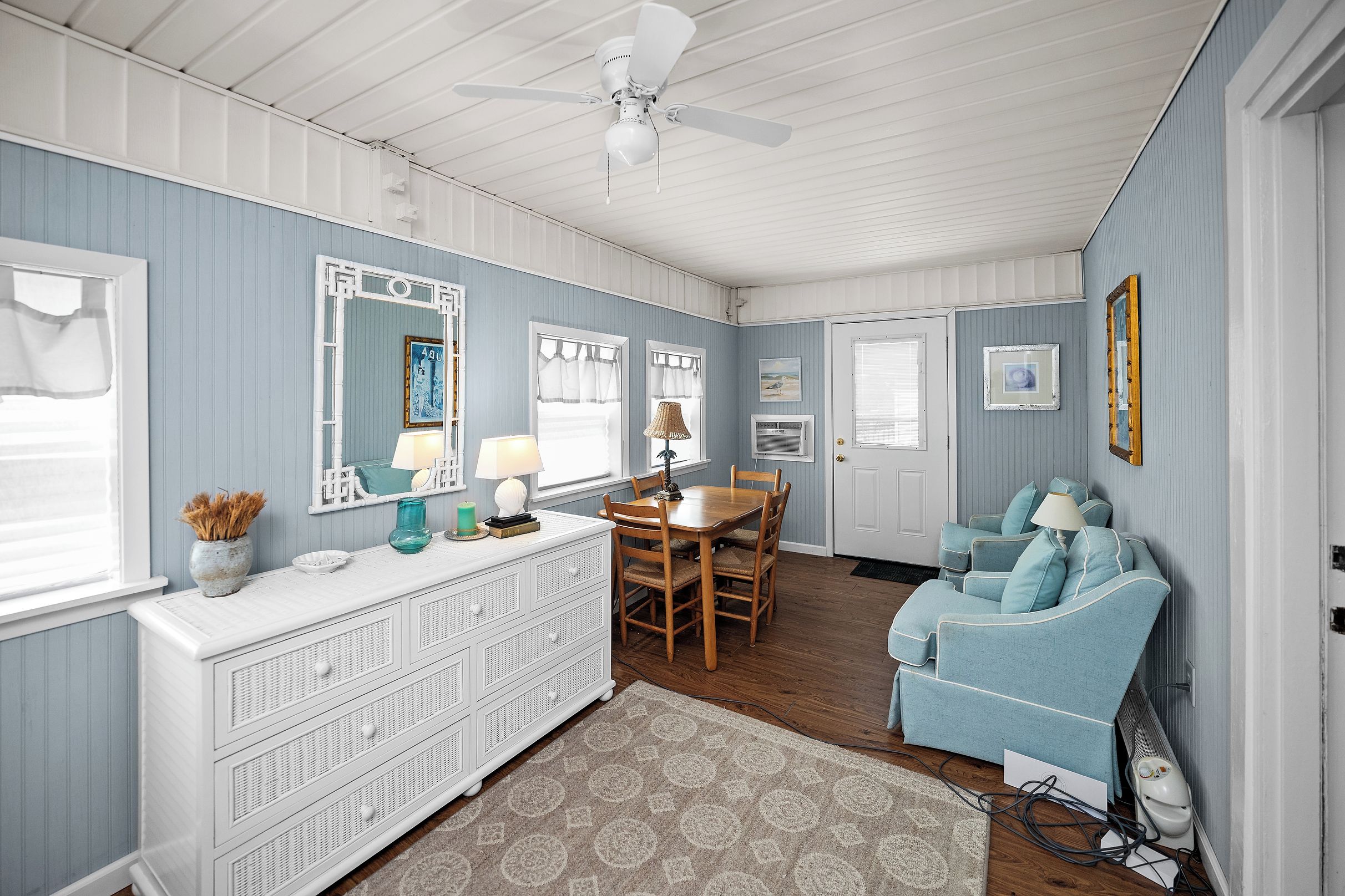 A room with a ceiling fan, a dining table with chairs, a sofa, and a window with curtains.