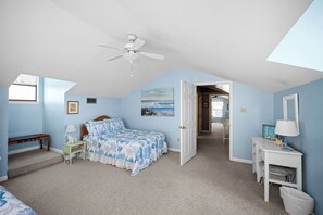 Een slaapkamer met een bed, een bureau, een stoel, een plafondventilator en een deur naar een andere kamer.
