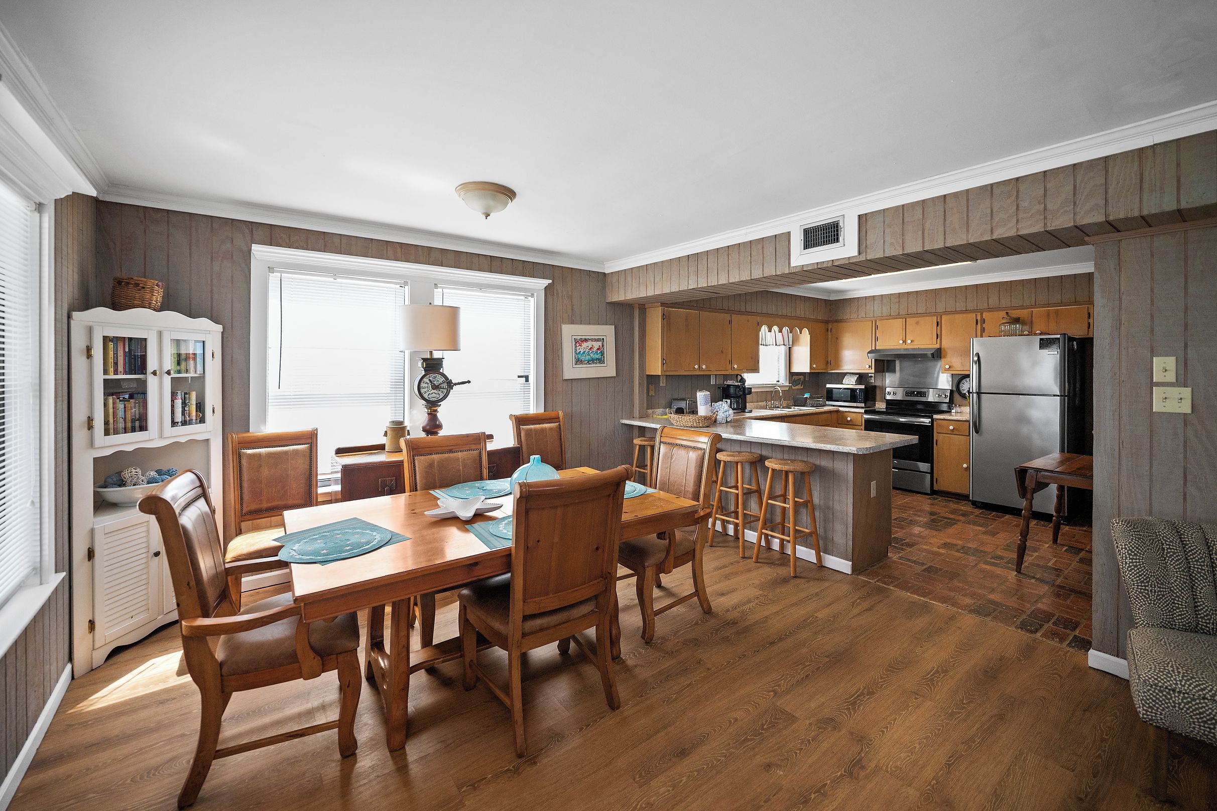 A modern kitchen with wooden cabinets, a central island, and a dining area with wooden chairs and a table.