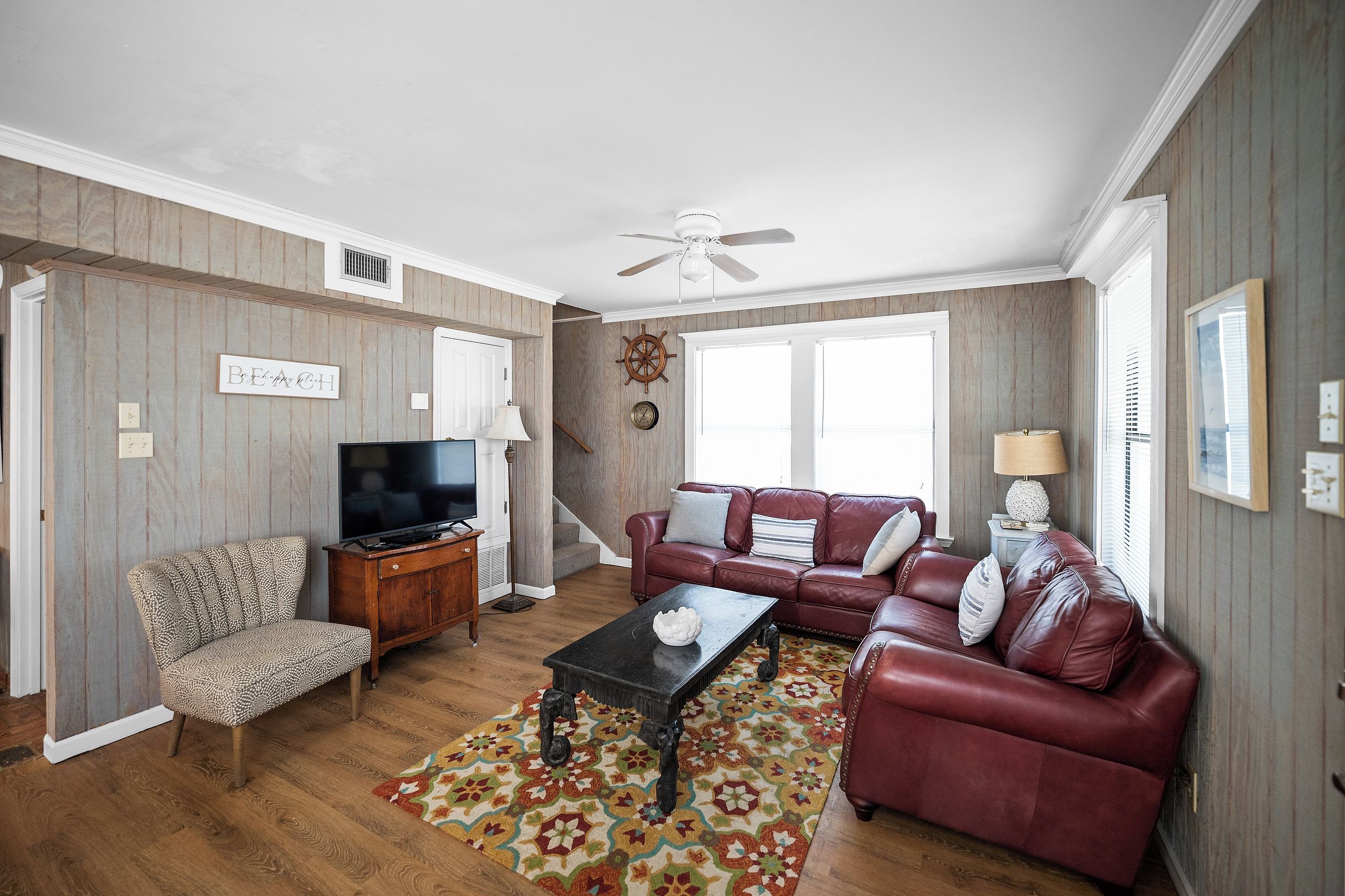 A living room with a television, a sofa, a patterned armchair, a coffee table, and a patterned rug.
