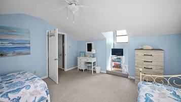 A bedroom with two beds, a desk, a dresser, a ceiling fan, and a beach-themed painting.