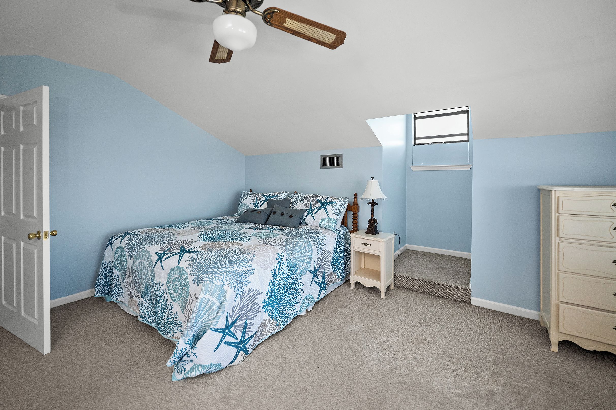 Un dormitorio con cama, mesita de noche, cómoda, ventilador de techo y ventana.