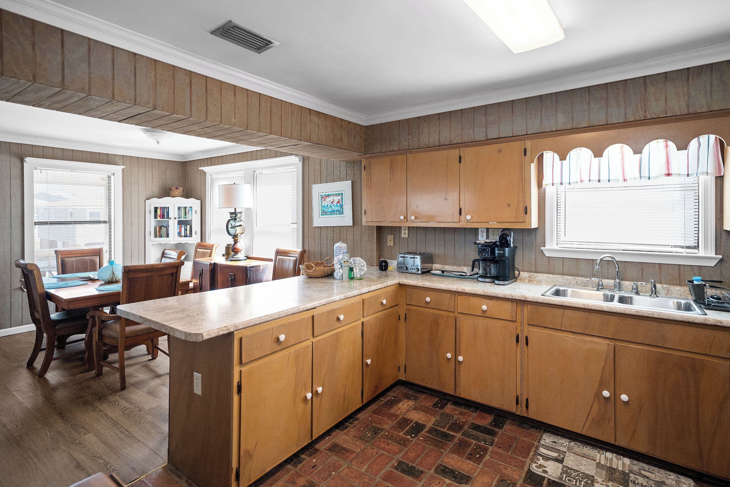 A kitchen with wooden cabinets, a dining area with a table and chairs, and a kitchen island with a sink and appliances.