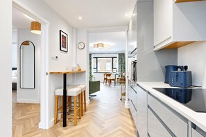 A modern kitchen with a built-in oven, a blue appliance on the counter, and a dining area with a table and chairs. - AC! Modern Flat, 5 mins from Angel - Pass the Keys (London)