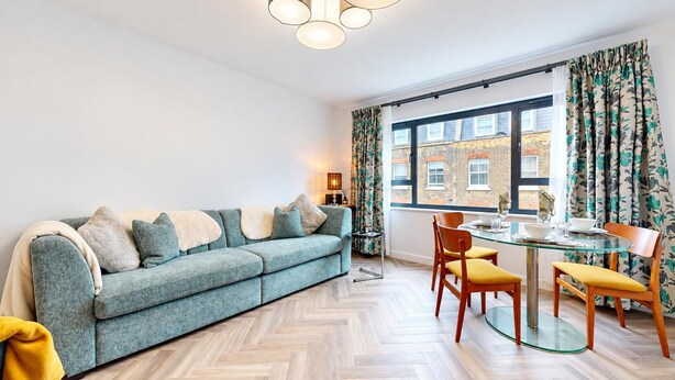 A modern living room with a sofa, a dining table with chairs, and a large window with curtains. - AC! Modern Flat, 5 mins from Angel - Pass the Keys (London)