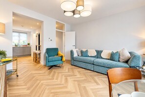A modern living room with a sofa, armchair, and a dining area with a glass table. - AC! Modern Flat, 5 mins from Angel - Pass the Keys (London)