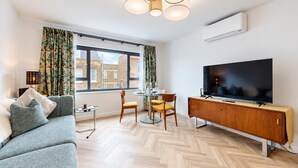 A modern living room with a sofa, TV, dining table, chairs, and a large window with curtains. - AC! Modern Flat, 5 mins from Angel - Pass the Keys (London)