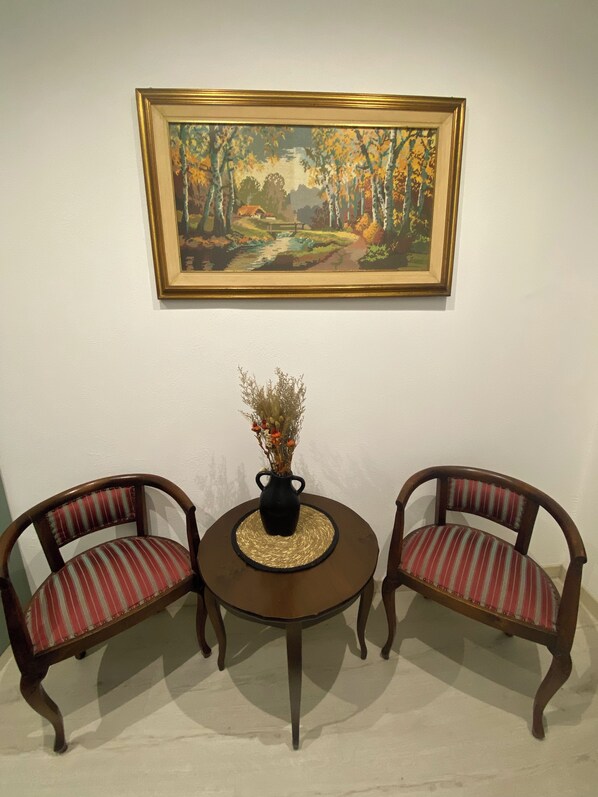 Un coin repas avec une table ronde, deux chaises rembourrées, un vase contenant des fleurs séchées et un tableau représentant un paysage, accroché au mur.