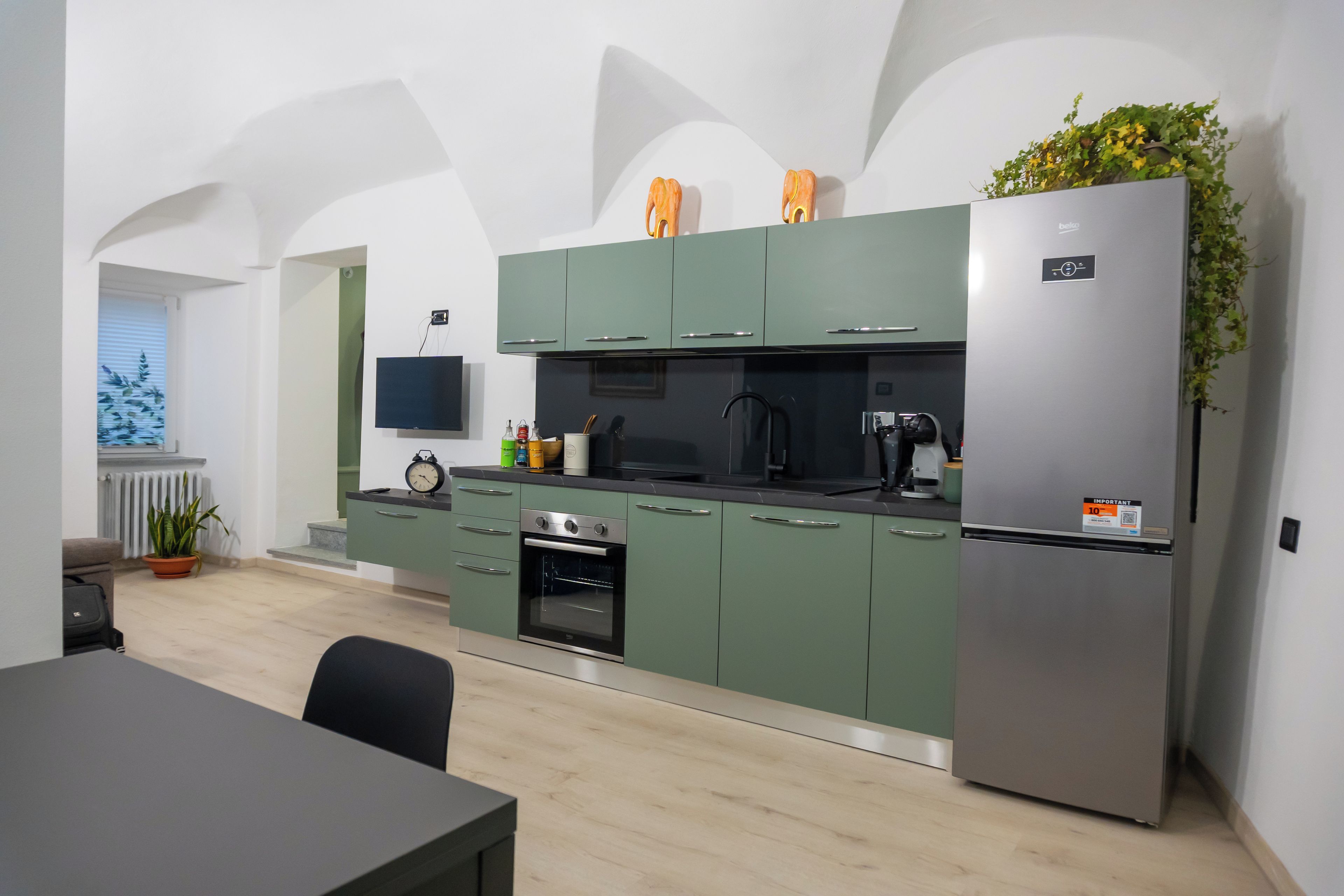 Una cocina moderna con gabinetes verdes, un refrigerador de acero inoxidable y un horno empotrado.
