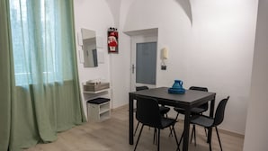 Ein Essbereich mit Tisch und Stühlen, einem grünen Vorhang, einer weißen Tür und einem kleinen Regal mit Gegenständen.