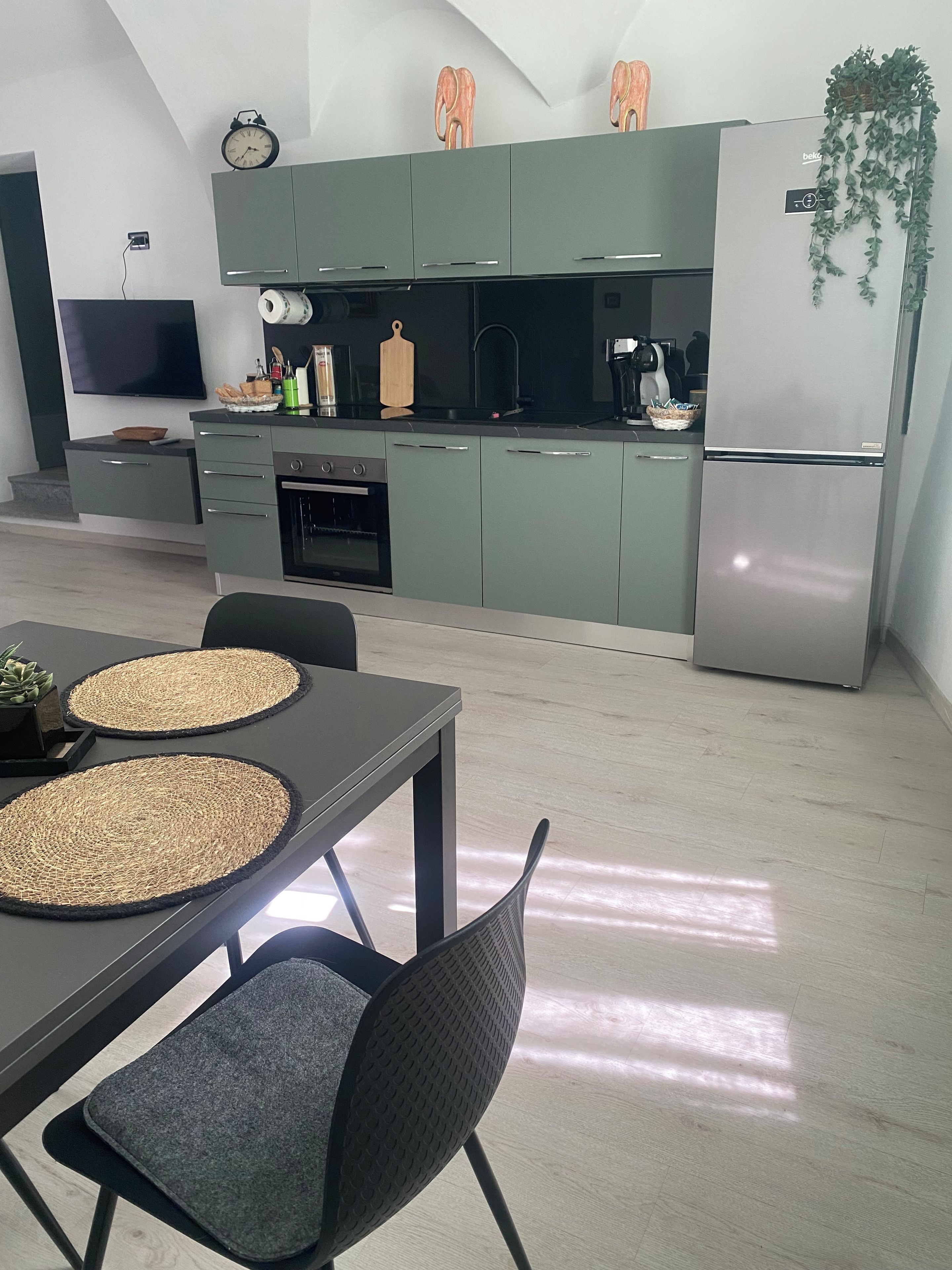 Een moderne keuken met grijze kastjes, een roestvrijstalen koelkast en een flatscreen televisie aan de wand.